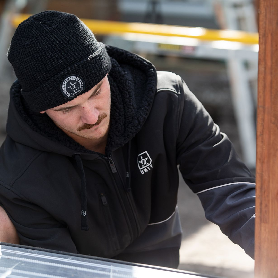 Person wearing a black beanie and black hoodie while working outdoors.