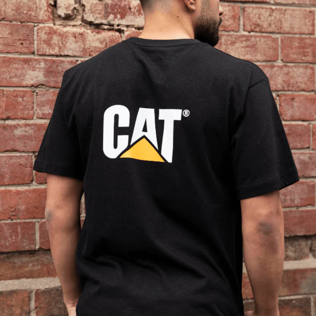 Person wearing a black CAT t-shirt standing against a brick wall.