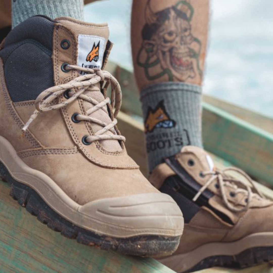 Close-up of tan work boots and grey socks with a tattoo visible on the leg.